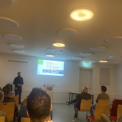 Presentatie op de muur met daarvoor mensen op stoelen die naar deze presentatie kijken