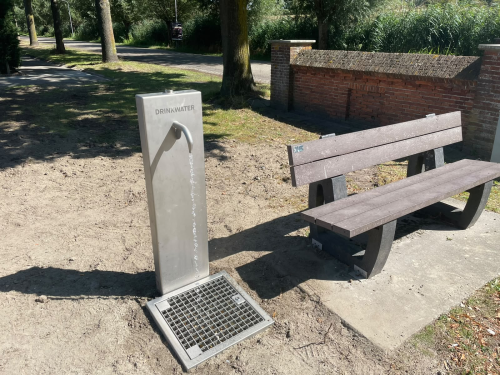 Watertappunt met een bankje ernaast in een groen perkje